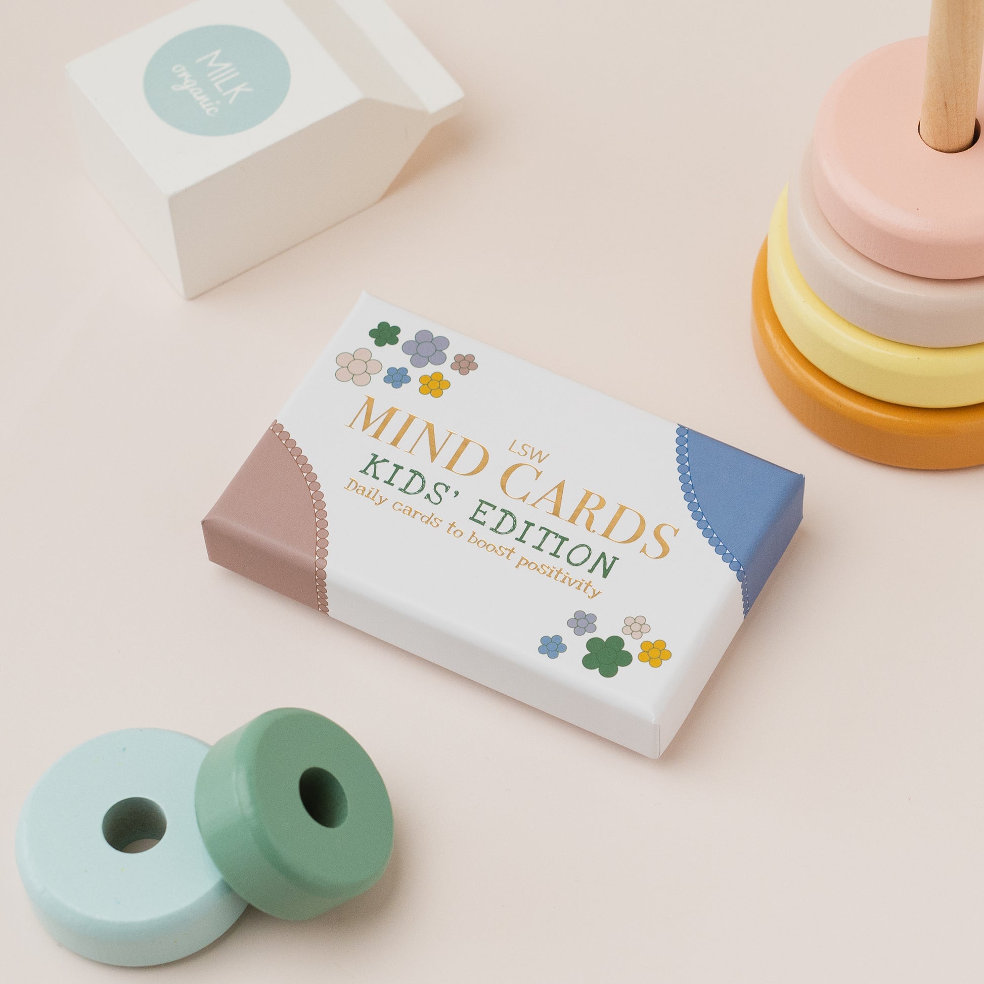 Box of 'Mind Cards Kids' Edition' on a light pink background with a stack of colorful wooden toys.